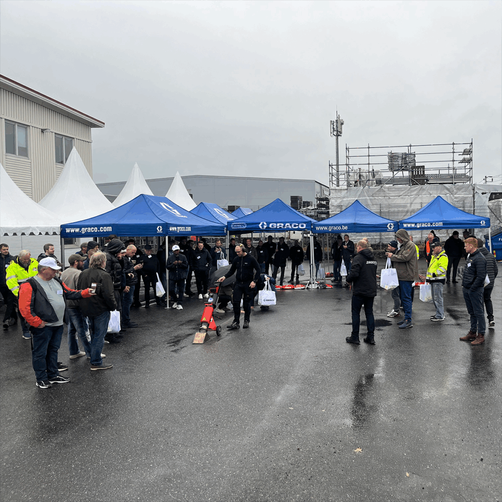 Mennesker på en parkeringsplass, utstillingstelt i bakgrunn, grå himmel